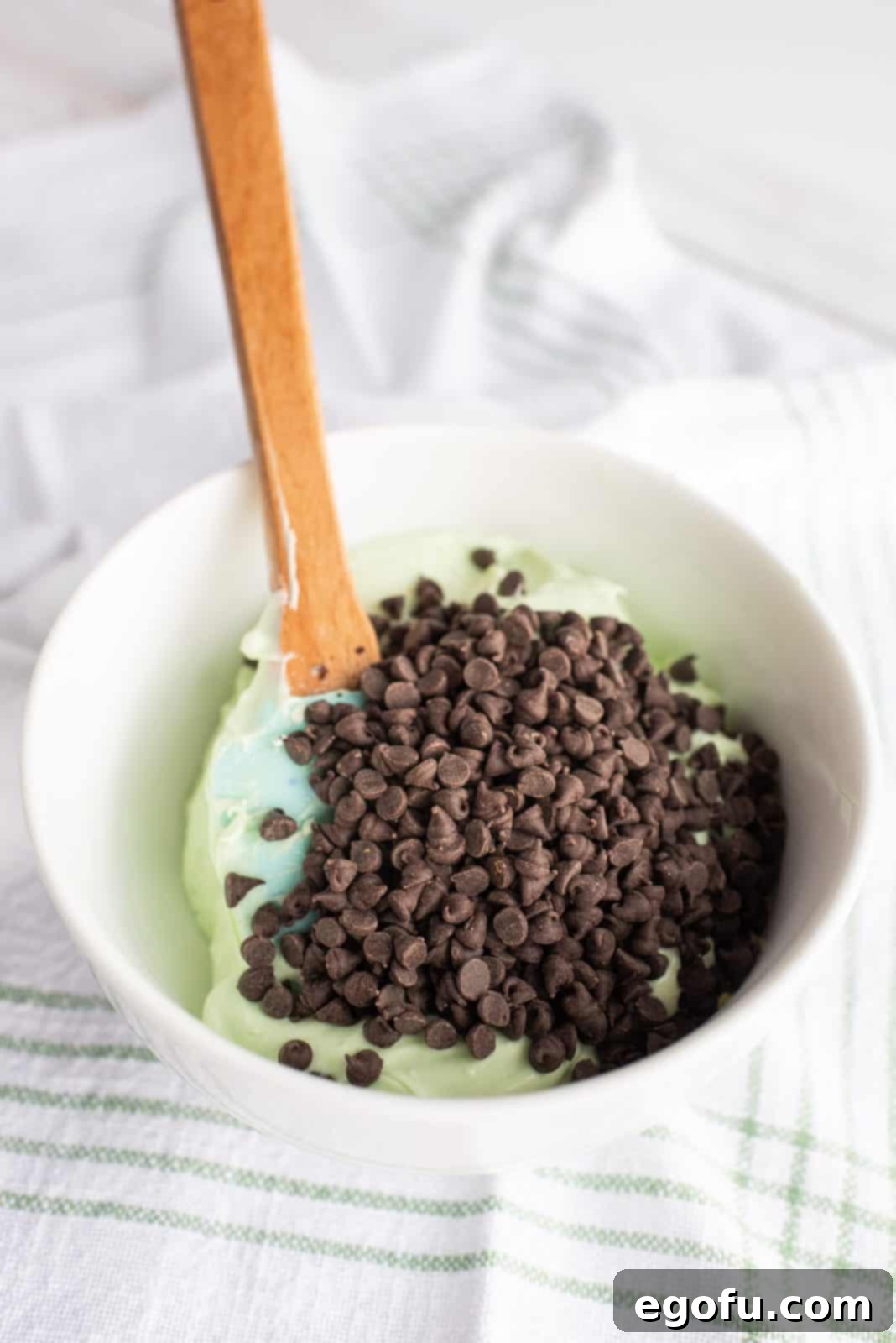 Chocolate chips being folded into the smooth mint cream cheese filling mixture.