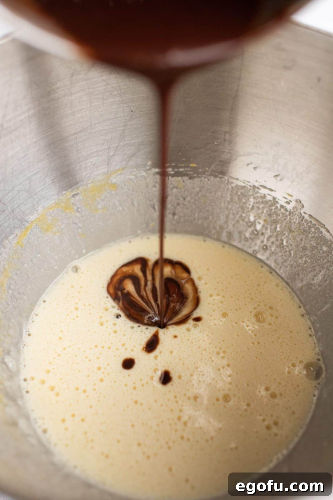 Melted chocolate mixture, sugar, vanilla, and eggs being beaten together in a stand mixer.