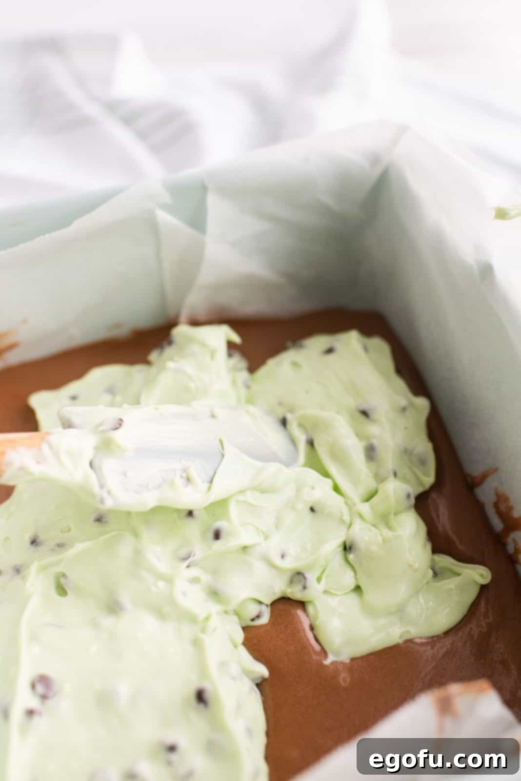 Mint cream cheese filling being carefully spread on top of the first brownie layer.