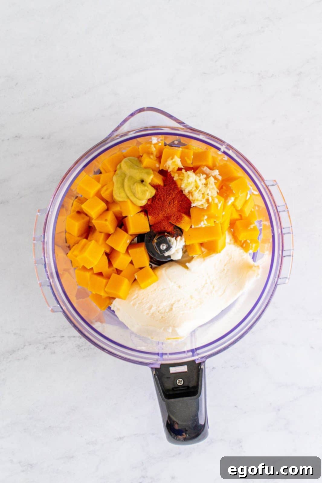 Cheddar, cream cheese, garlic, Worcestershire, dijon, and paprika in a food processor, ready to be blended.
