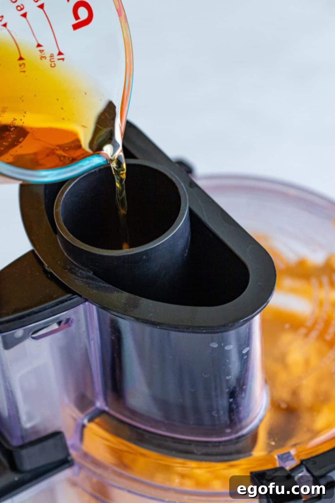 Beer being streamed into food processor into cheese mixture, illustrating the process of creating a smooth dip.