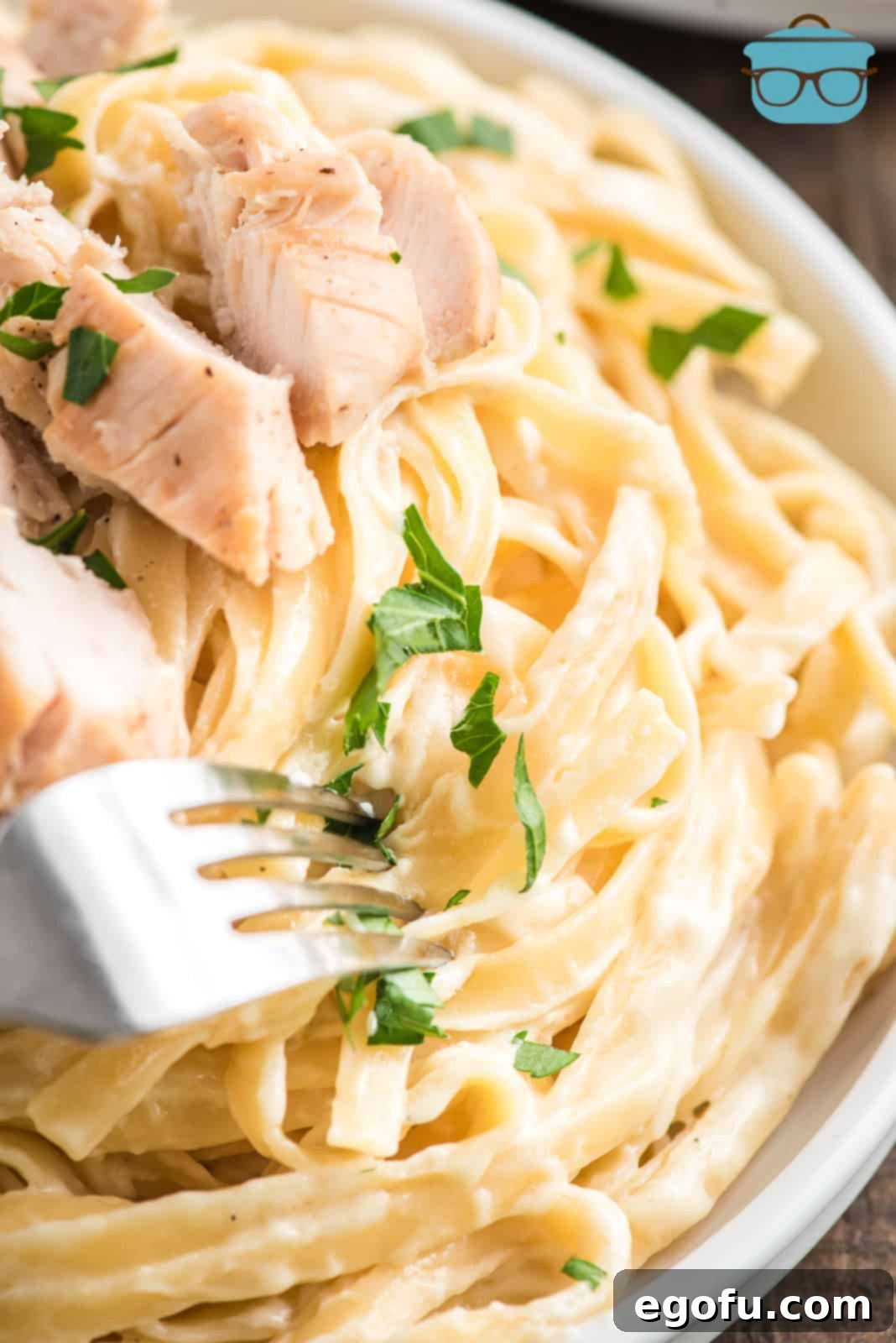 Close up of Copycat Olive Garden Chicken Alfredo in bowl with fork, showcasing creamy sauce and tender chicken.