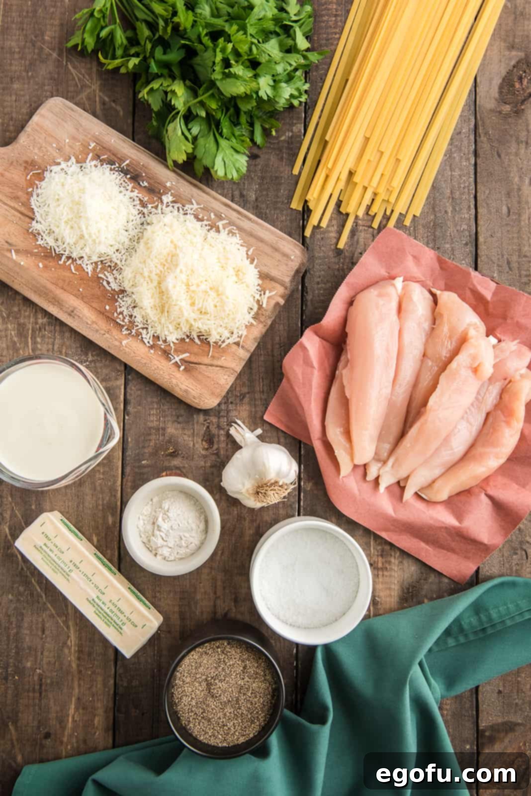 Array of fresh ingredients including fettuccine, chicken tenderloins, butter, garlic, flour, heavy cream, parmesan, romano cheese, salt, pepper, and parsley, ready for making Copycat Olive Garden Chicken Alfredo.