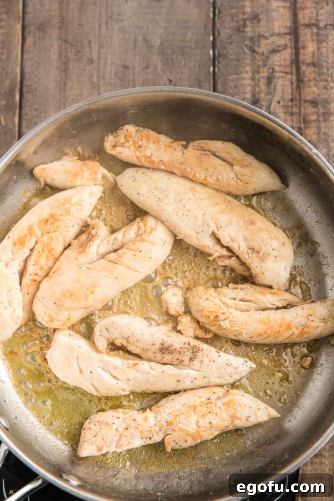 Chicken tenderloins sizzling and browning in a hot skillet with melted butter.