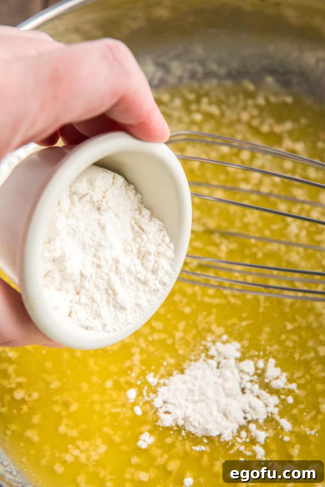 All-purpose flour being whisked into melted butter and fragrant minced garlic in a skillet.