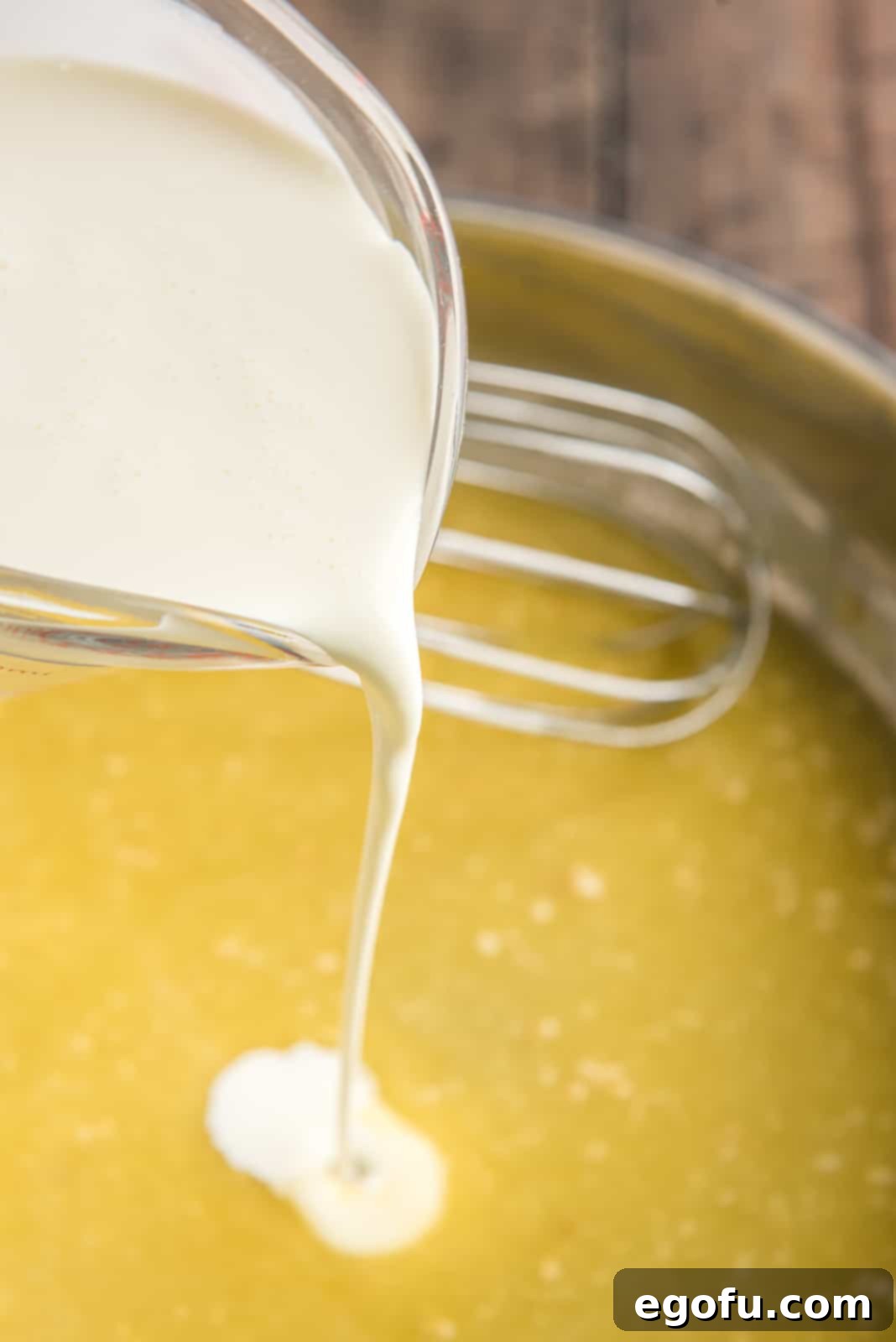 Heavy cream being slowly poured into the butter and flour mixture in a skillet, while being whisked.