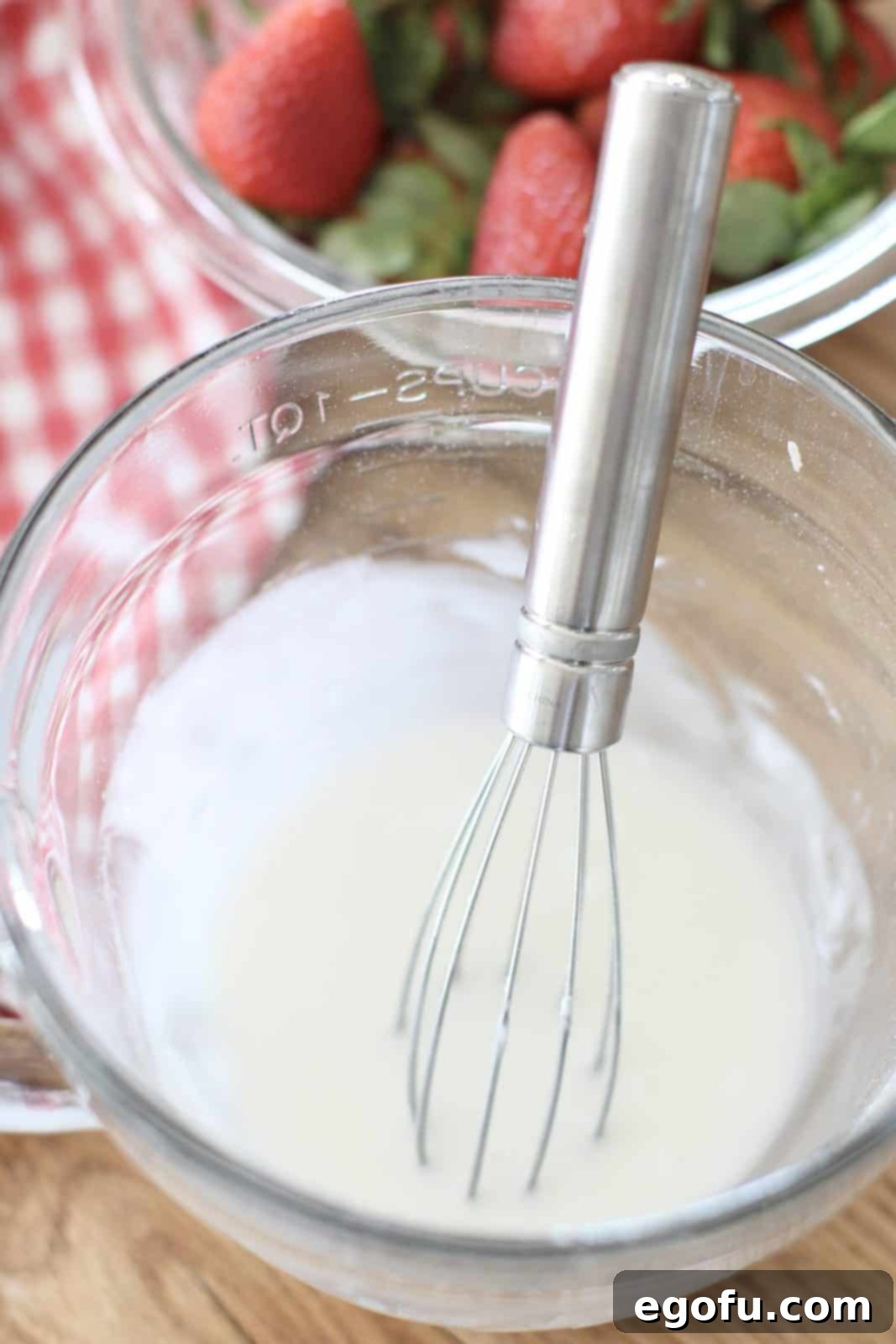 A smooth, white powdered sugar and milk glaze, subtly infused with strawberry extract, whisked to perfection in a small measuring bowl, ready to adorn the warm biscuits.