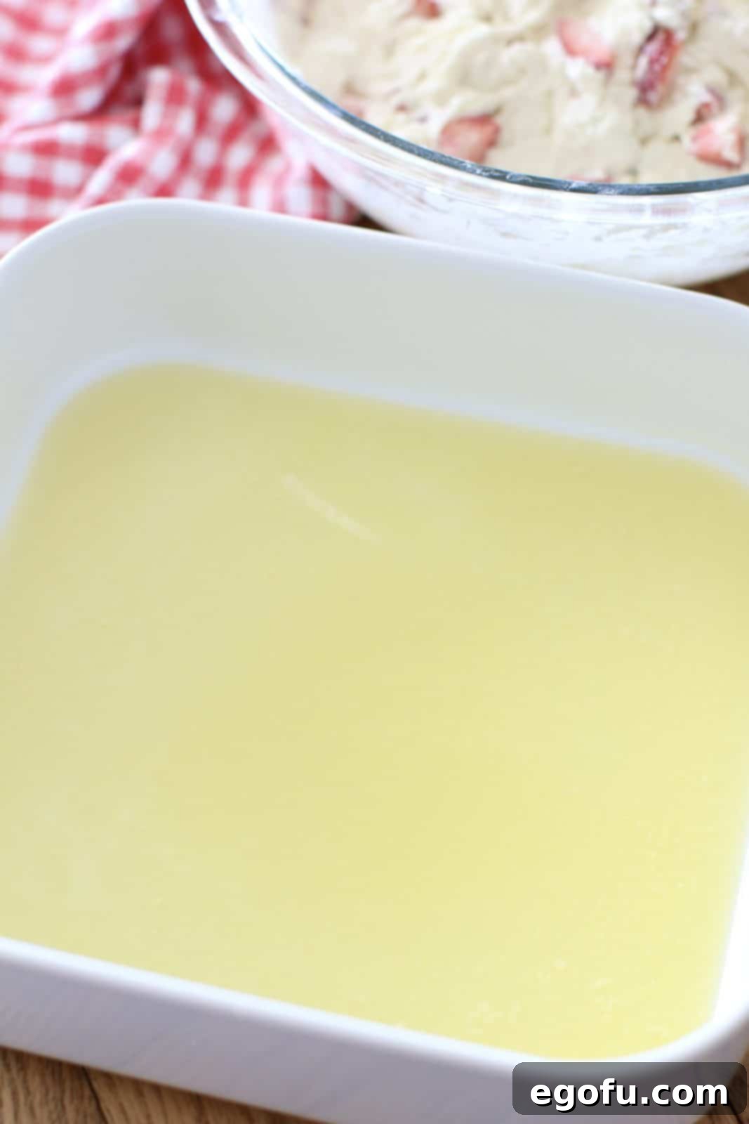 Melted golden butter pooling at the bottom of a pristine white square baking dish, ready to welcome the biscuit dough.