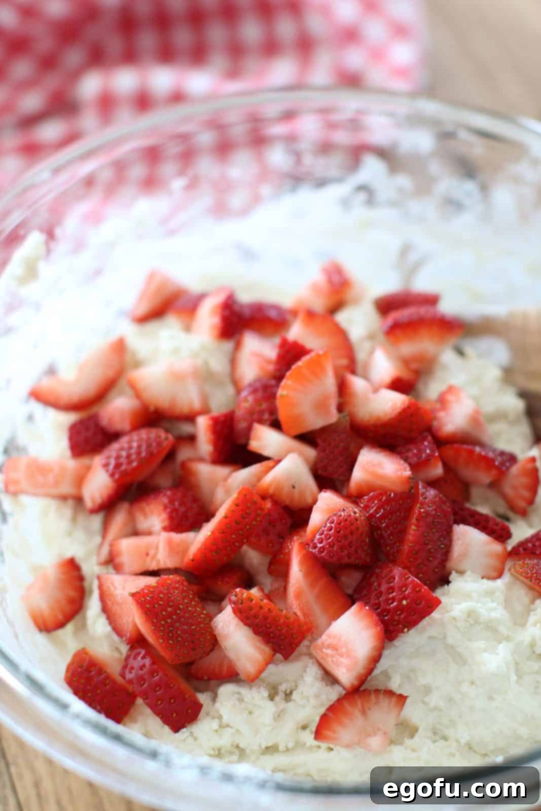 Freshly chopped strawberries gently incorporated into the sticky biscuit dough within a clear glass bowl, adding color and flavor.