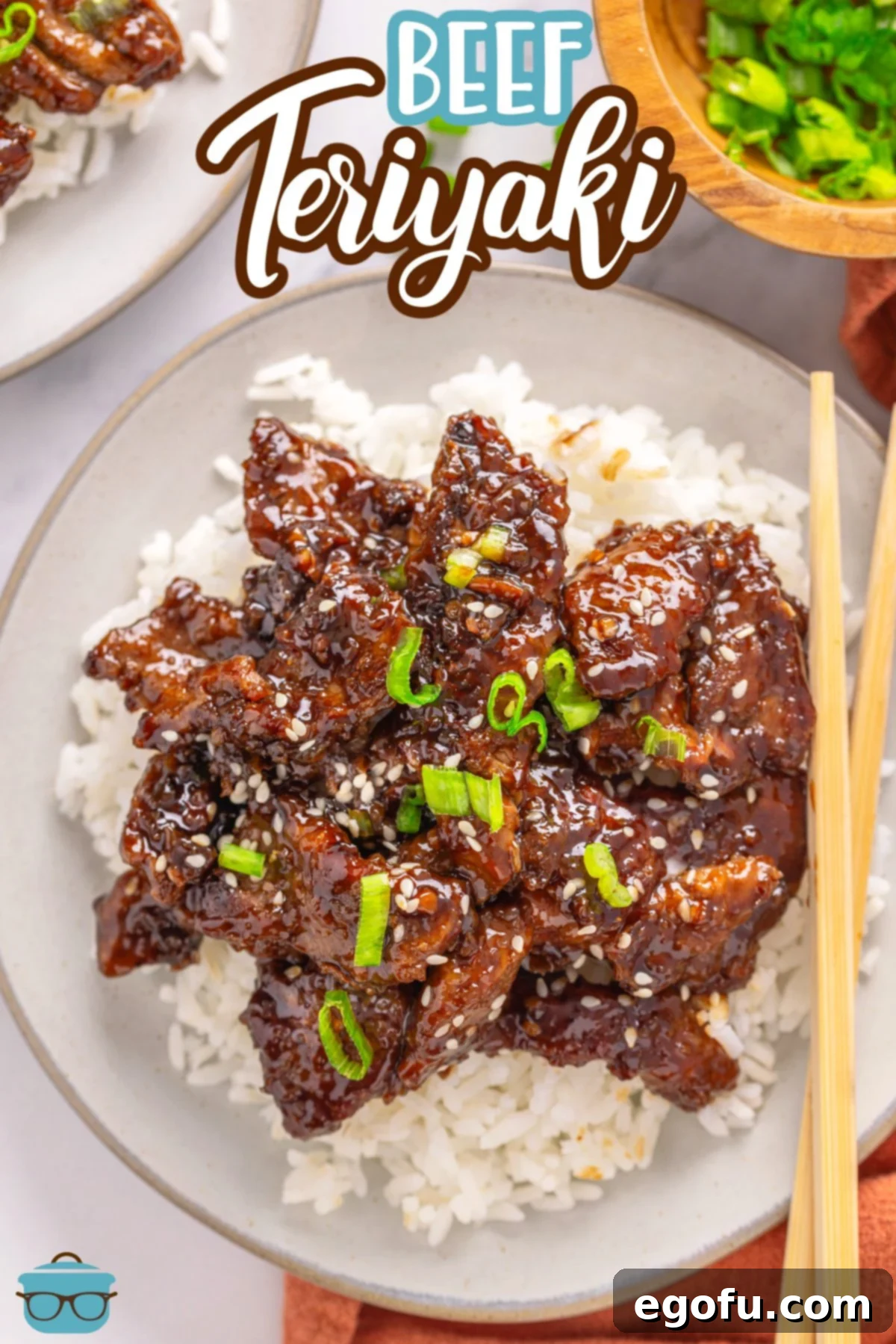 A tempting plate of Beef Teriyaki served over white rice with green onions and chopsticks.