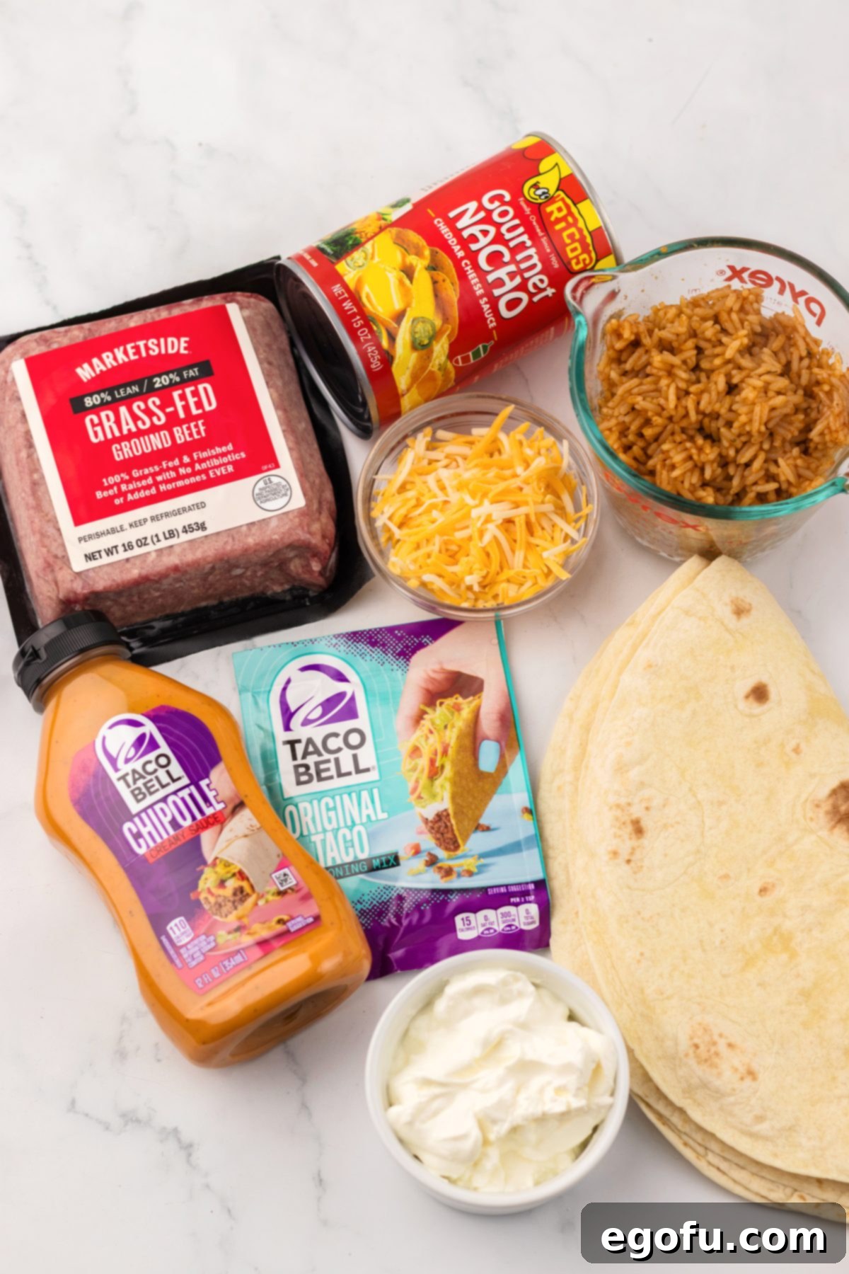 The essential ingredients for making a Taco Bell Quesarito at home: ground beef, taco seasoning, water, flour tortillas, shredded cheese, cooked rice, nacho cheese, sour cream, and chipotle sauce.