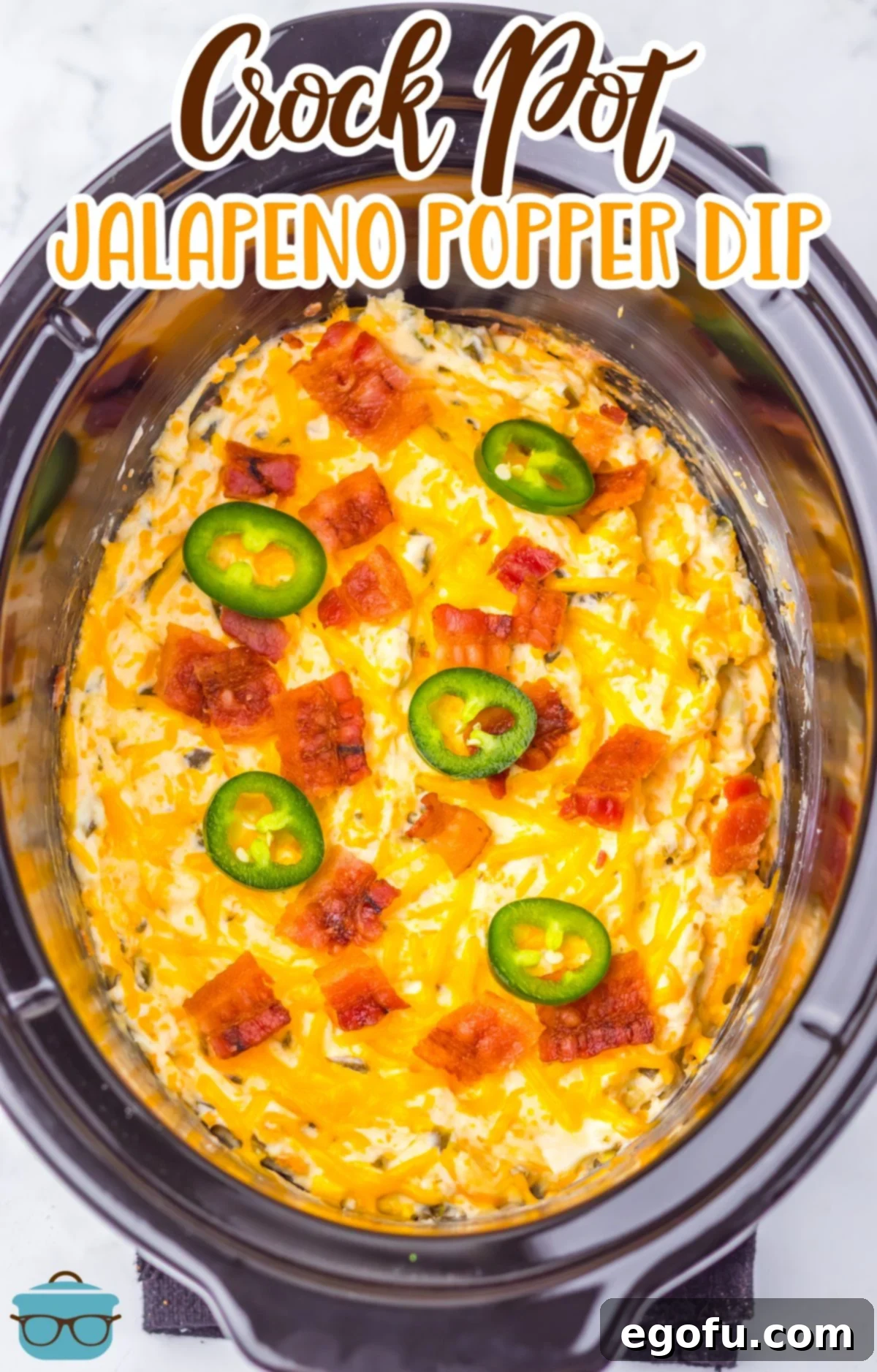 A slow cooker filled to the brim with Jalapeno Popper Dip, generously topped with crispy bacon and diced jalapeños.