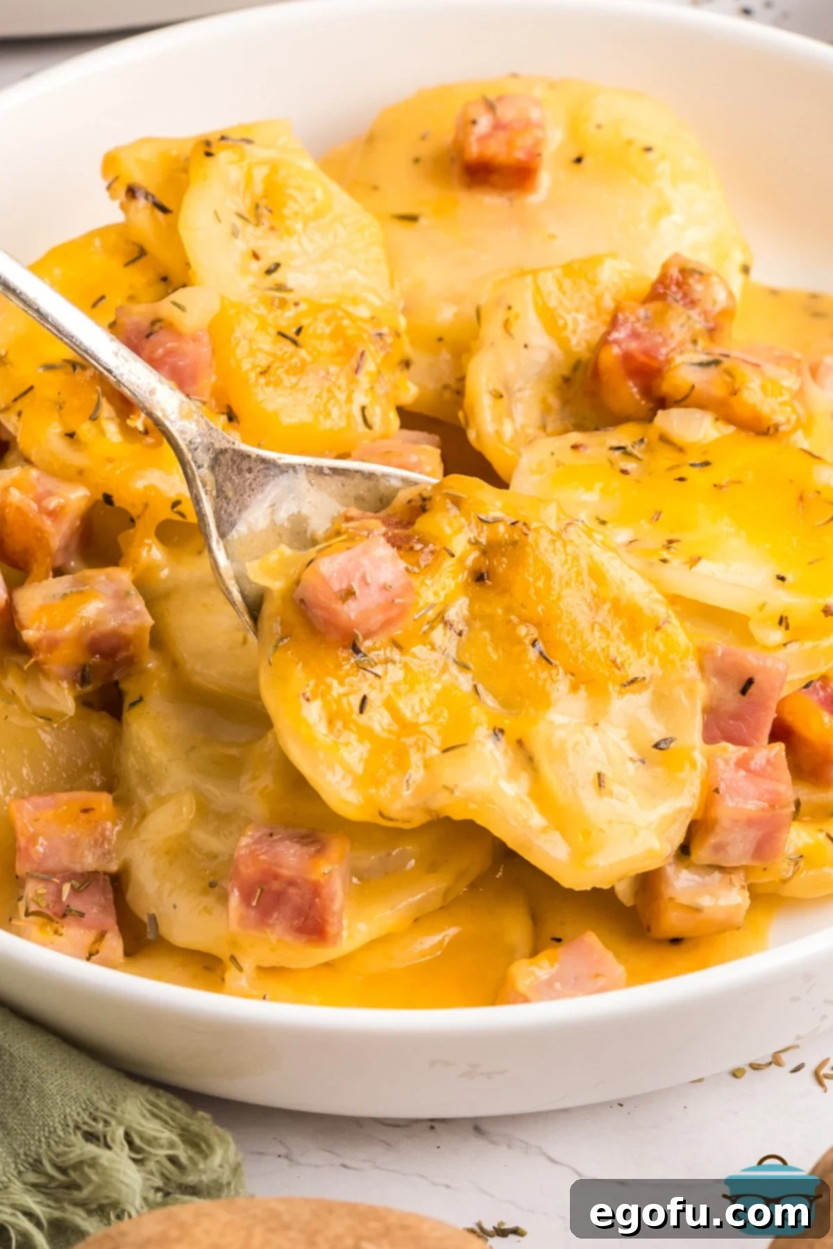 Slow Cooker Ham and Potatoes 2 Close-up shot of a utensil scooping a bite of creamy Crock Pot Ham and Potatoes from a serving bowl, showcasing the texture and deliciousness of the dish.