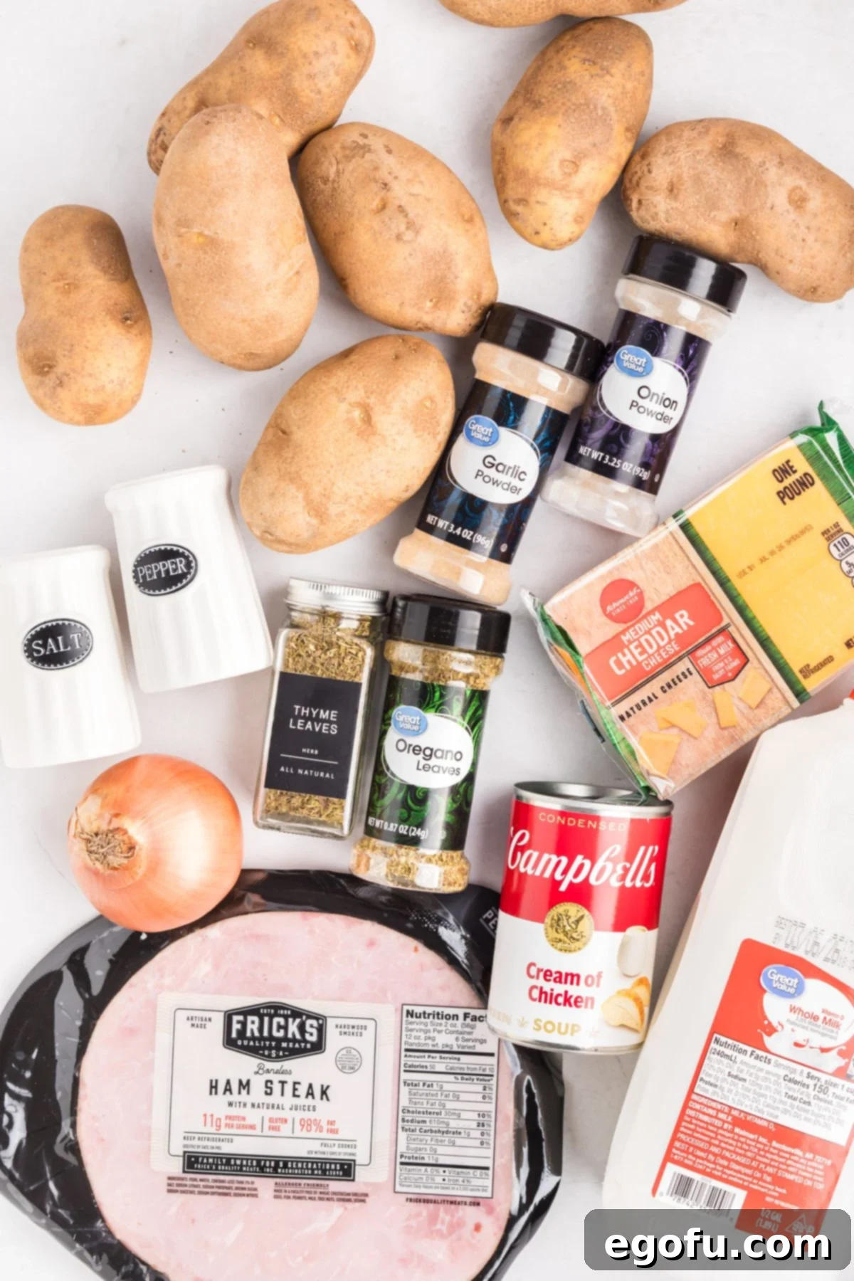 Slow Cooker Ham and Potatoes 4 An overhead shot showcasing all the ingredients needed for Crock Pot Ham and Potatoes: russet potatoes, salt, diced yellow onion, diced ham, shredded cheddar cheese, cream of chicken soup, whole milk, dried thyme, oregano, onion powder, garlic powder, and black pepper.